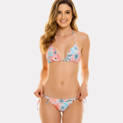 Mujer sonriendo de perfil con bikini reversible estampado tropical rosado y celeste, top triangular y amarre lateral en la cadera.