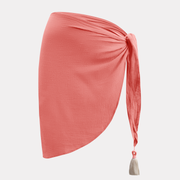 Pareo coral visto de perfil con diseño asimétrico y detalle de borla blanca.