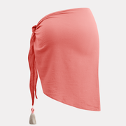 Pareo coral corto para mujer con amarre lateral y borla decorativa blanca.