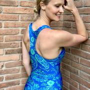 Vista posterior del traje de baño estampado azul con verde, modelo apoyada en pared de ladrillos.