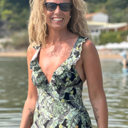 Mujer sonriendo usando traje de baño entero con control de abdomen y estampado tropical.