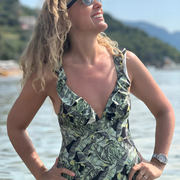 Mujer en la playa con traje de baño estampado tropical de hojas verdes y escote profundo.